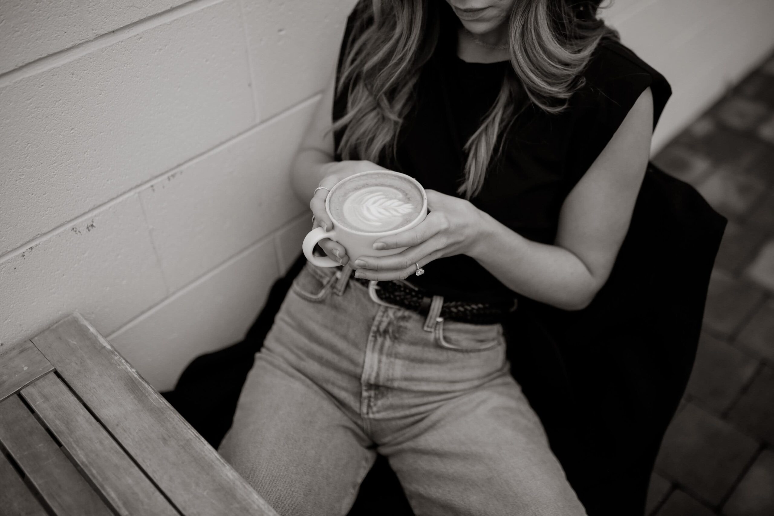 Black and white image of girl in jeans and tank holding a coffee.